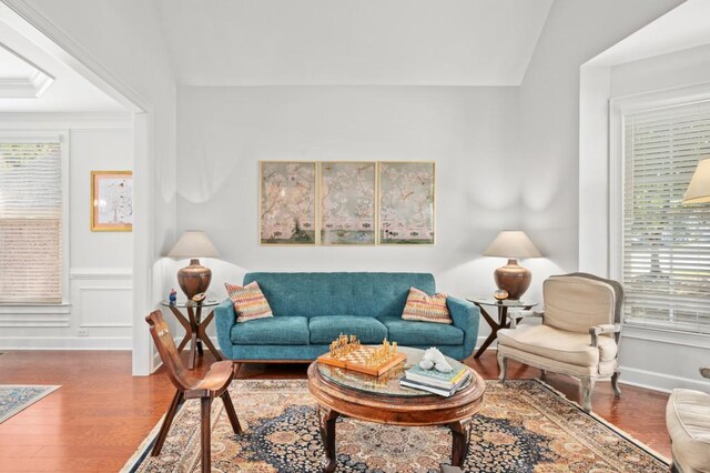 living room with wood-type flooring, ornamental molding, and vaulted ceiling