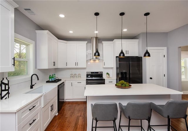 kitchen with wall chimney range hood, decorative light fixtures, black appliances, and a center island