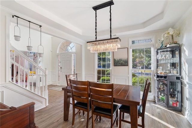 dining room featuring a wainscoted wall, stairs, a tray ceiling, and wood finished floors