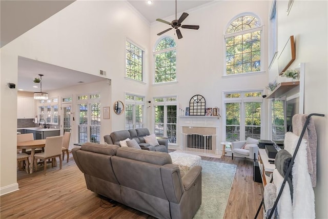 living area with visible vents, light wood-style floors, ornamental molding, a fireplace with flush hearth, and ceiling fan