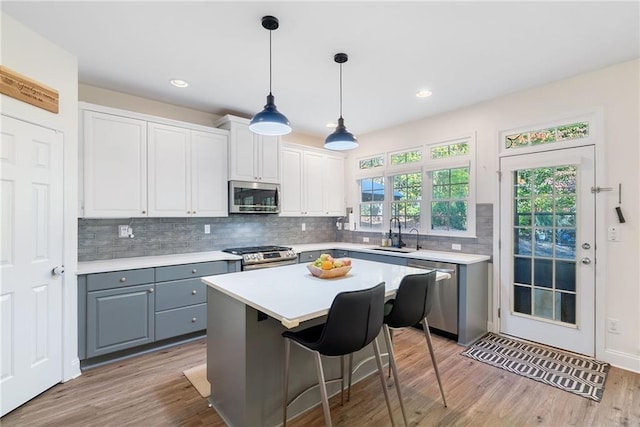 kitchen featuring gray cabinetry, stainless steel appliances, a sink, light countertops, and decorative backsplash