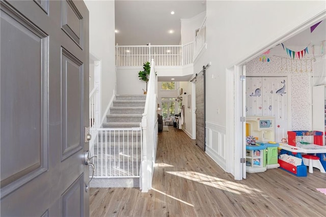 foyer with a wainscoted wall, stairway, a high ceiling, a barn door, and wood finished floors