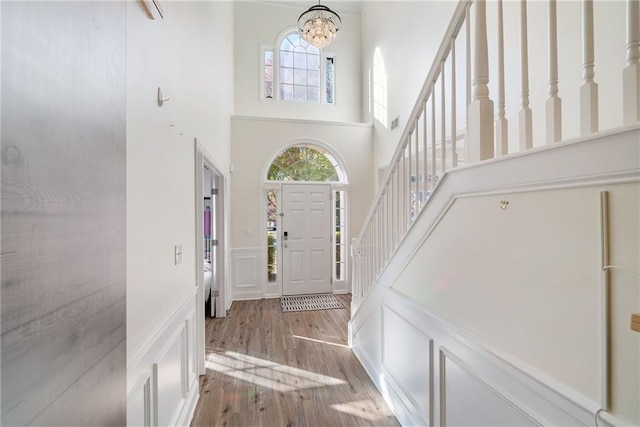 foyer featuring a notable chandelier, a decorative wall, wood finished floors, a towering ceiling, and stairs