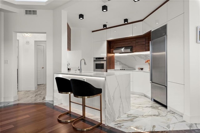 kitchen featuring visible vents, marble finish floor, appliances with stainless steel finishes, wall chimney exhaust hood, and modern cabinets