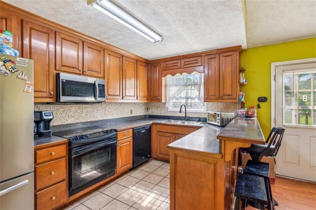 60 Boardwalk Ave, Covington, GA 30016 - kitchen with black appliances, a peninsula, a breakfast bar, brown cabinets, and a textured ceiling