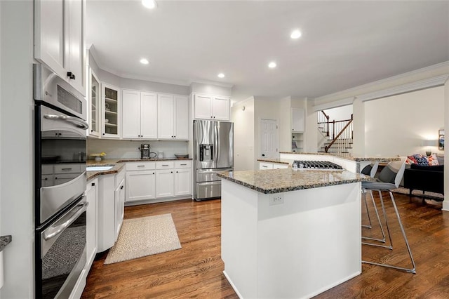 3714 Westbrooke Cir NE, Brookhaven, GA 30319 - kitchen with stainless steel appliances, crown molding, a breakfast bar area, white cabinetry, and glass insert cabinets