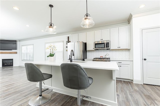 kitchen with white cabinets, appliances with stainless steel finishes, hanging light fixtures, and an island with sink