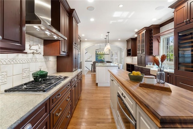 kitchen featuring arched walkways, wall chimney exhaust hood, a kitchen island, butcher block countertops, and stainless steel gas stovetop