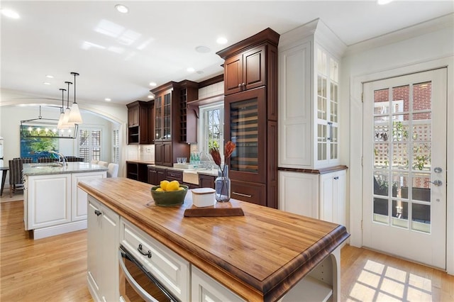 kitchen featuring light wood-style floors, a wealth of natural light, glass insert cabinets, and an island with sink