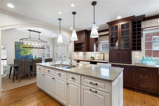 kitchen featuring arched walkways, backsplash, light wood-style floors, glass insert cabinets, and a sink