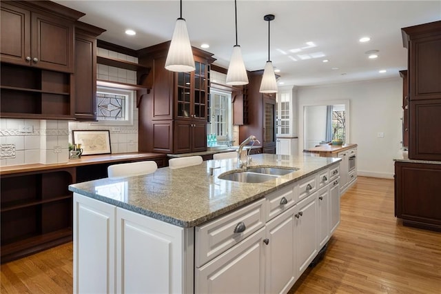 kitchen featuring open shelves, a sink, a center island with sink, and a healthy amount of sunlight