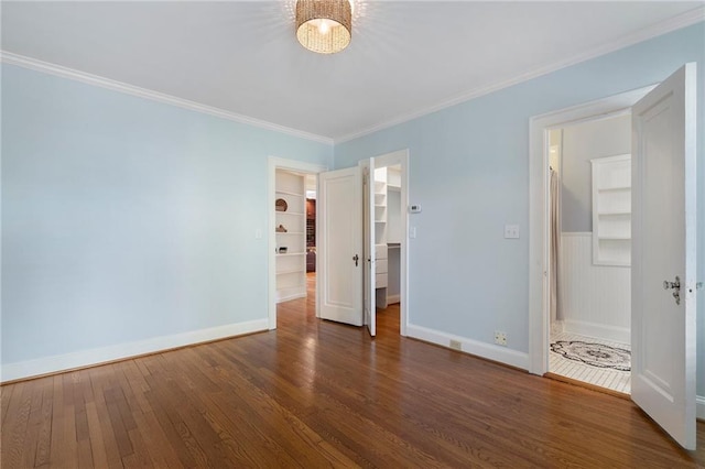 unfurnished bedroom with baseboards, a spacious closet, hardwood / wood-style floors, and crown molding