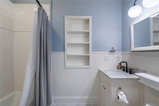 full bath with a wainscoted wall, a sink, shower / bath combo with shower curtain, and built in features