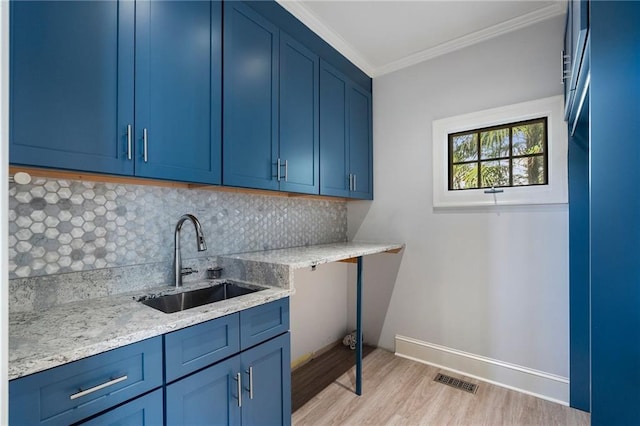 kitchen with a sink, blue cabinetry, decorative backsplash, light wood finished floors, and crown molding