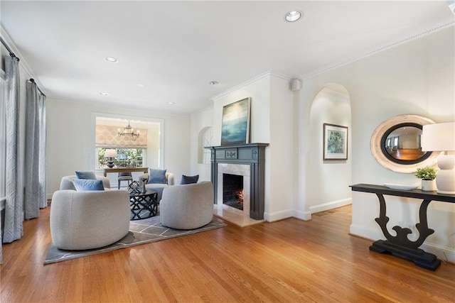 living area with a chandelier, wood finished floors, a high end fireplace, baseboards, and ornamental molding