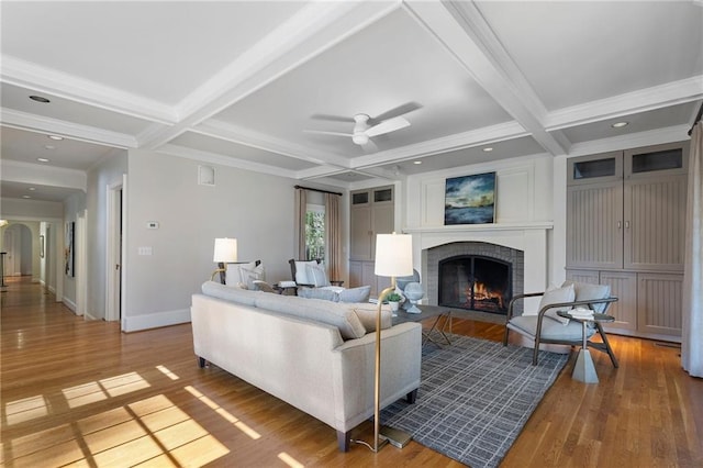 living room with a brick fireplace, coffered ceiling, beam ceiling, and wood finished floors