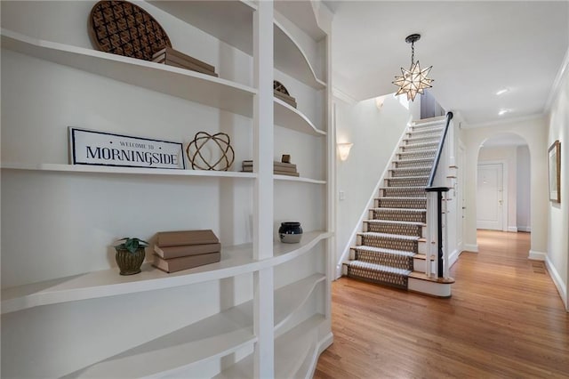 entrance foyer featuring baseboards, arched walkways, wood finished floors, stairs, and crown molding