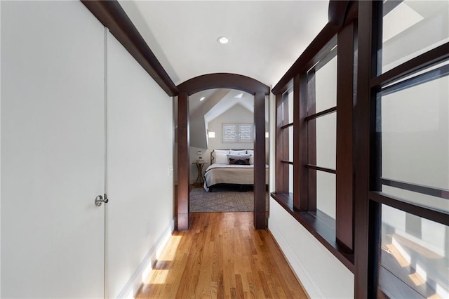 corridor featuring lofted ceiling, light wood-style floors, arched walkways, and recessed lighting