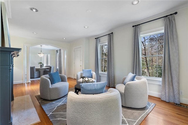 living area featuring arched walkways, crown molding, recessed lighting, and wood finished floors