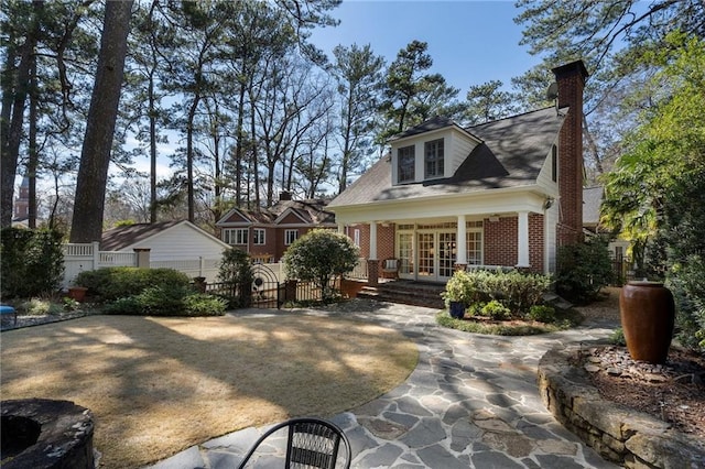 view of front of property featuring a fenced front yard, french doors, brick siding, a chimney, and a gate