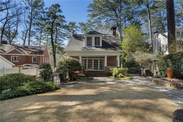 view of front facade featuring french doors, brick siding, fence, and a chimney