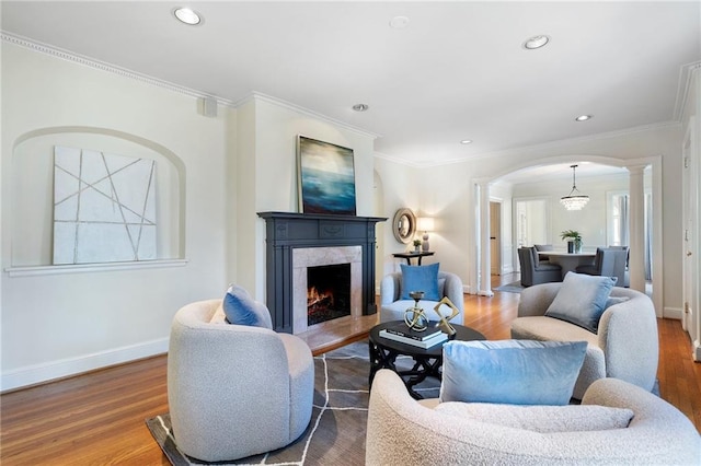 living area featuring decorative columns, baseboards, arched walkways, wood finished floors, and a high end fireplace