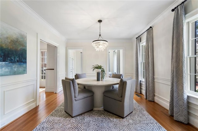 dining room with ornamental molding, a chandelier, a decorative wall, and wood finished floors