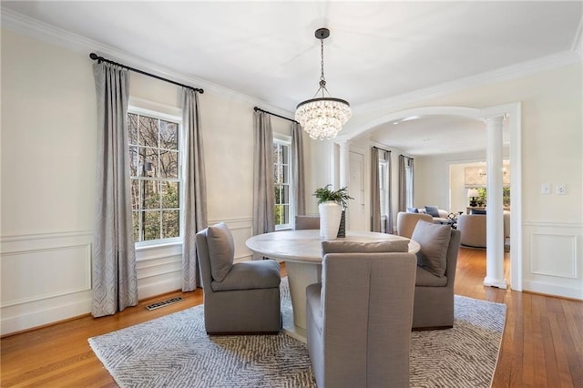 dining area with arched walkways, a decorative wall, visible vents, wood-type flooring, and decorative columns