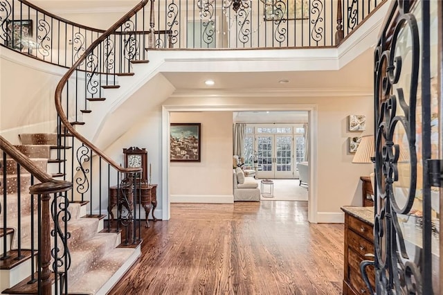 foyer entrance featuring hardwood / wood-style floors, a towering ceiling, and ornamental molding