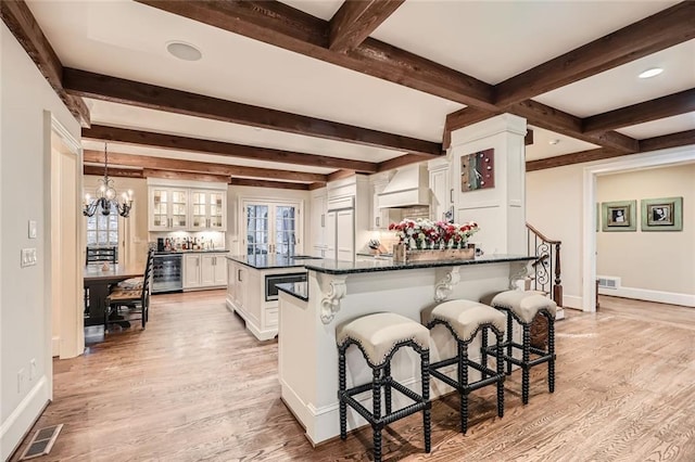 kitchen with a kitchen breakfast bar, custom exhaust hood, beverage cooler, decorative light fixtures, and white cabinets