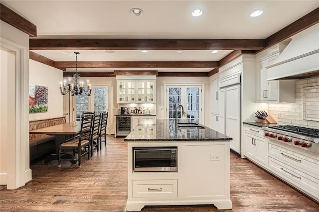 kitchen with sink, built in appliances, dark stone countertops, wine cooler, and an island with sink