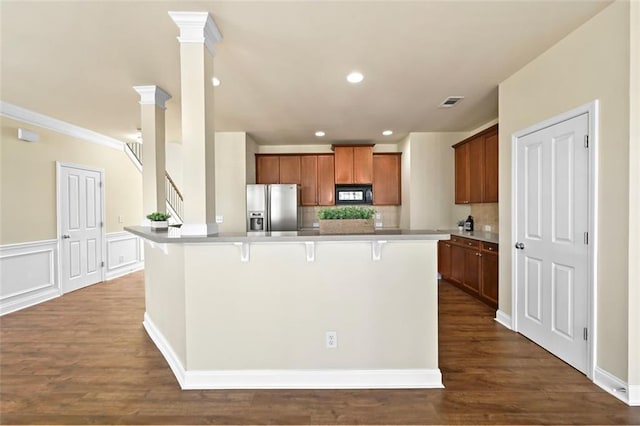 kitchen with black microwave, a breakfast bar, stainless steel refrigerator with ice dispenser, brown cabinets, and a center island with sink