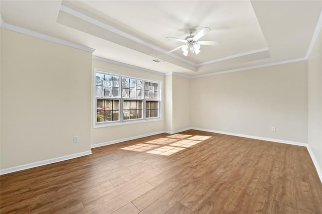 spare room with baseboards, a raised ceiling, ceiling fan, ornamental molding, and wood finished floors