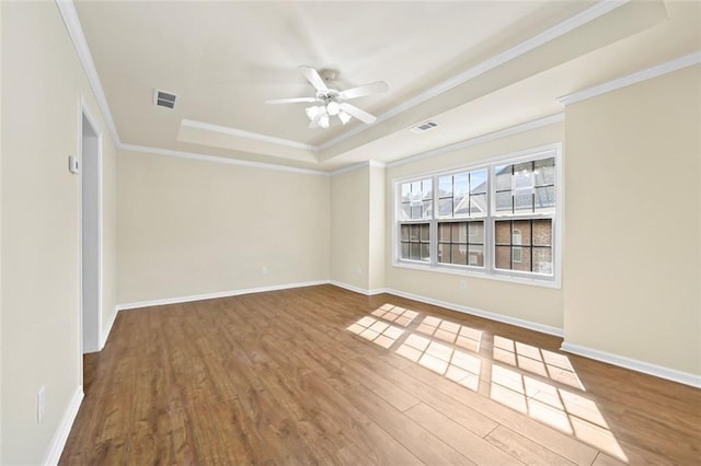 spare room with ceiling fan, wood finished floors, baseboards, a raised ceiling, and crown molding