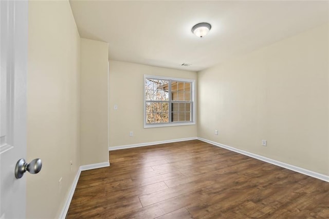 spare room featuring dark wood-type flooring, visible vents, and baseboards