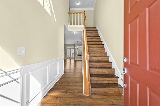 staircase with a decorative wall, a high ceiling, wood finished floors, ornamental molding, and wainscoting