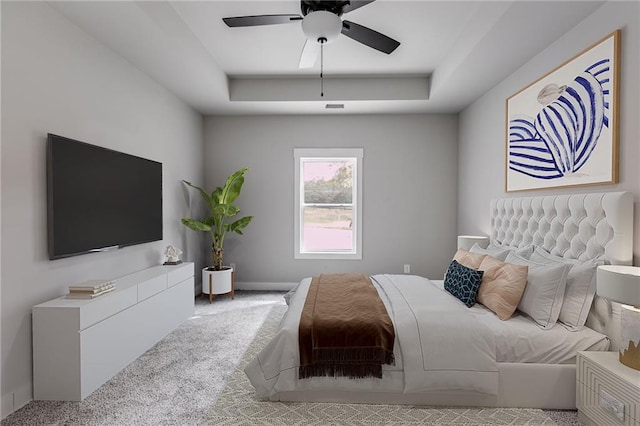 carpeted bedroom with a tray ceiling, baseboards, and ceiling fan