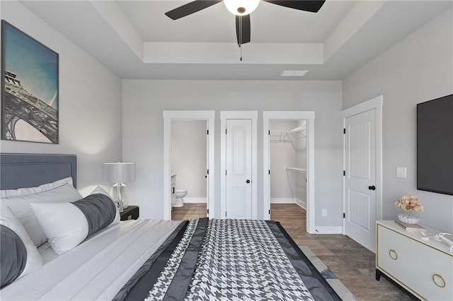 bedroom with wood finished floors, a tray ceiling, a spacious closet, and ensuite bath