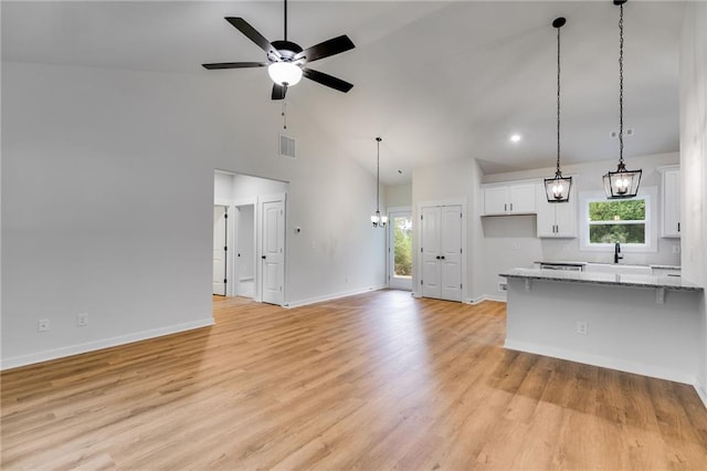 unfurnished living room featuring ceiling fan, healthy amount of natural light, baseboards, high vaulted ceiling, and light wood finished floors