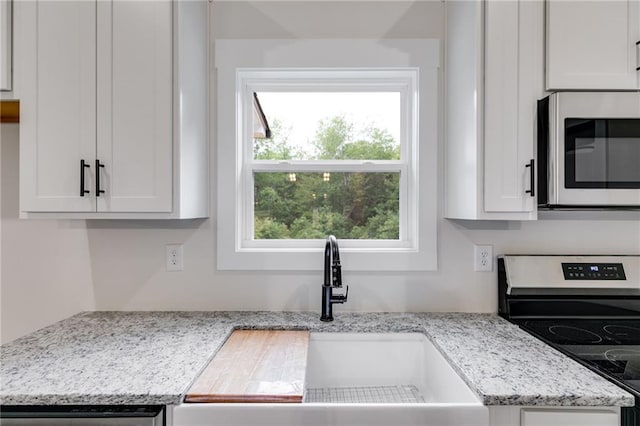 kitchen with stainless steel appliances, a sink, white cabinetry, and light stone countertops