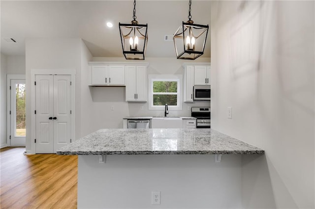 kitchen with appliances with stainless steel finishes, white cabinetry, a kitchen bar, light stone countertops, and light wood-type flooring