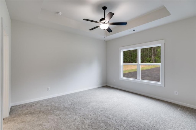empty room with a tray ceiling, carpet, baseboards, and ceiling fan