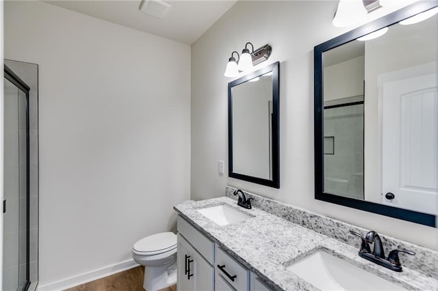 bathroom featuring wood finished floors, a shower with shower door, toilet, double vanity, and baseboards