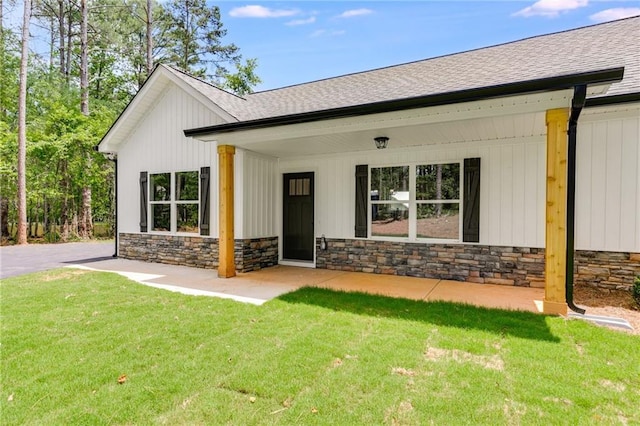 view of front of home with roof with shingles, stone siding, and a front lawn