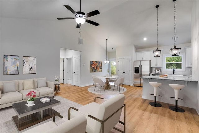 living area with light wood finished floors, plenty of natural light, a ceiling fan, high vaulted ceiling, and recessed lighting