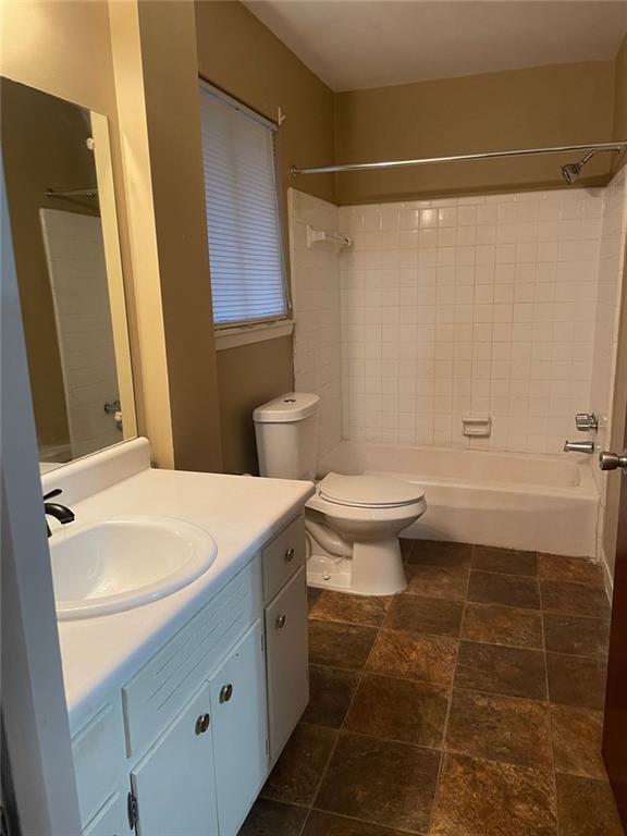 bathroom with stone finish floor, shower / tub combination, vanity, and toilet