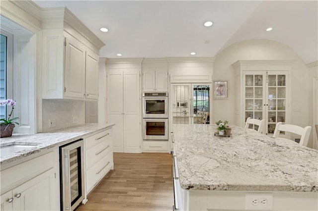 kitchen with a breakfast bar area, backsplash, wine cooler, light stone counters, and stainless steel double oven