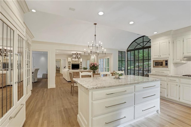 kitchen featuring light stone countertops, a center island, stainless steel microwave, and light wood-type flooring