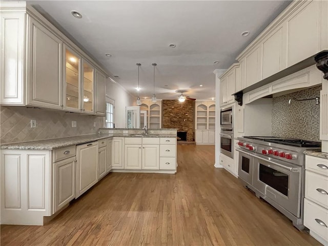 kitchen with appliances with stainless steel finishes, hanging light fixtures, kitchen peninsula, ceiling fan, and decorative backsplash