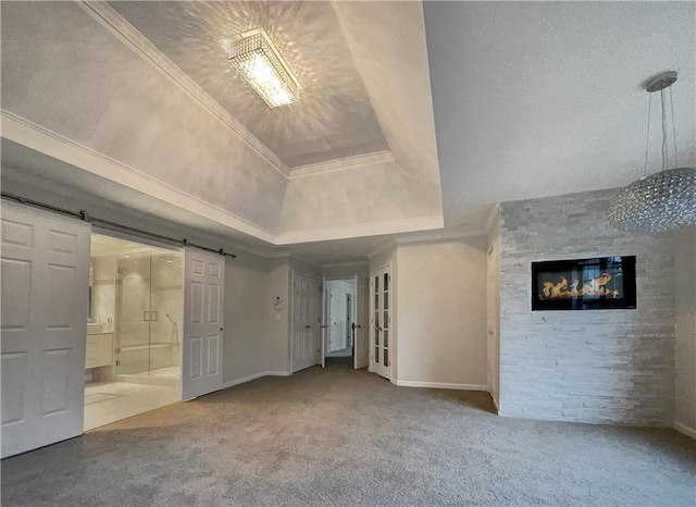 unfurnished living room featuring a raised ceiling, a barn door, crown molding, carpet flooring, and a high ceiling